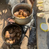 Pots of cooked meat outdoors served beside small bowls and buns