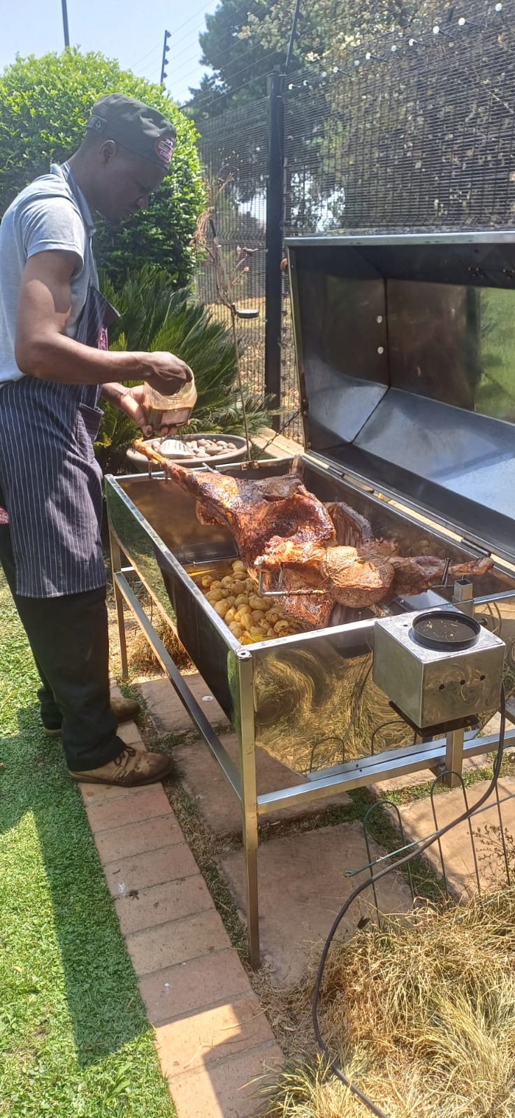 Our chef basting a whole lamb on the spit with baby potatoes
