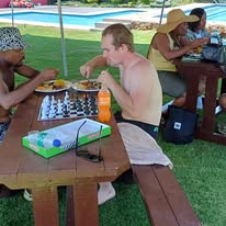Guests playing chess with plates of food by the pool